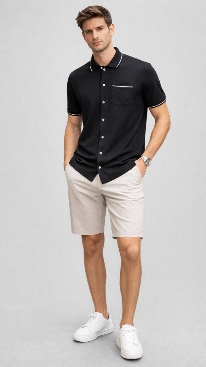 Man wearing a black shirt with white trim and beige shorts on a gray background