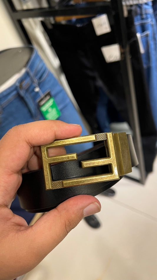 Gold and black belt buckle held in a hand with a blurred store background