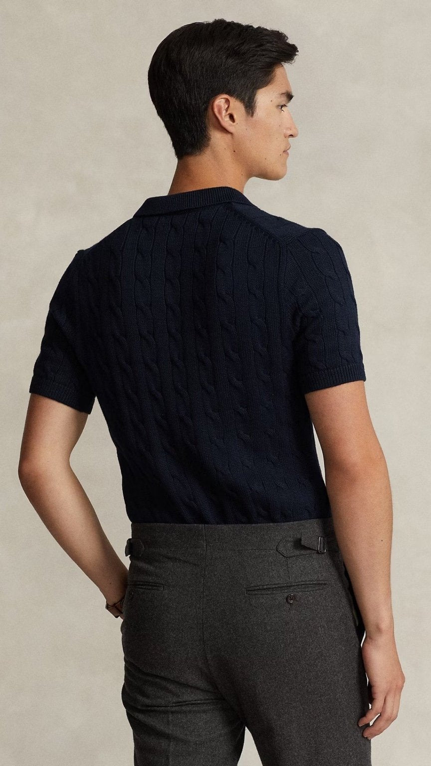 Man wearing a dark blue textured polo shirt and gray pants against a beige background