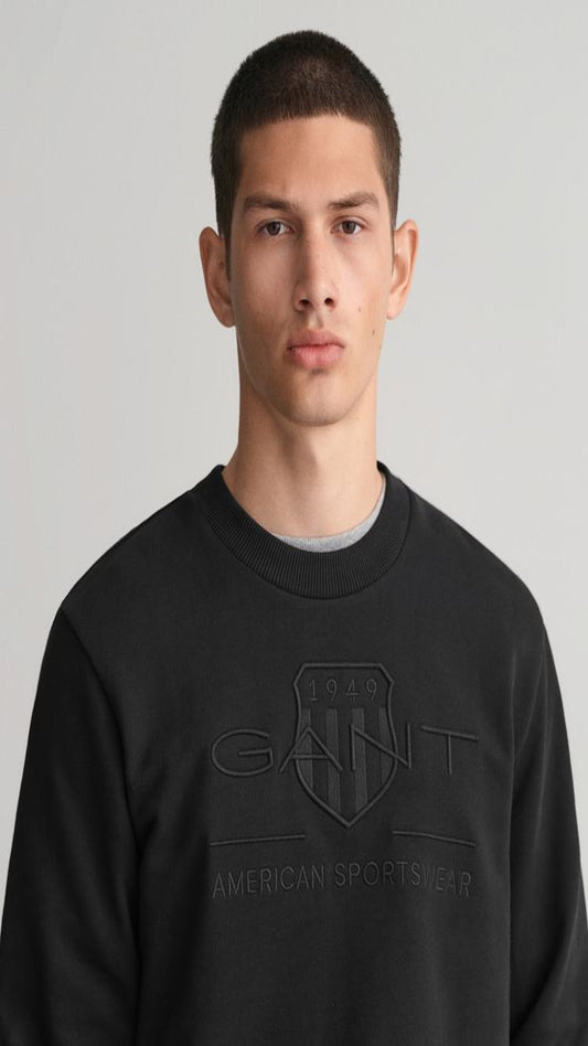Person wearing a black Gant sweatshirt against a plain background