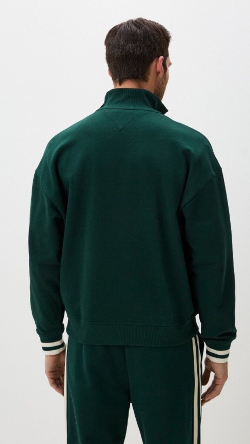 Man wearing a green tracksuit with white stripes on a light gray background