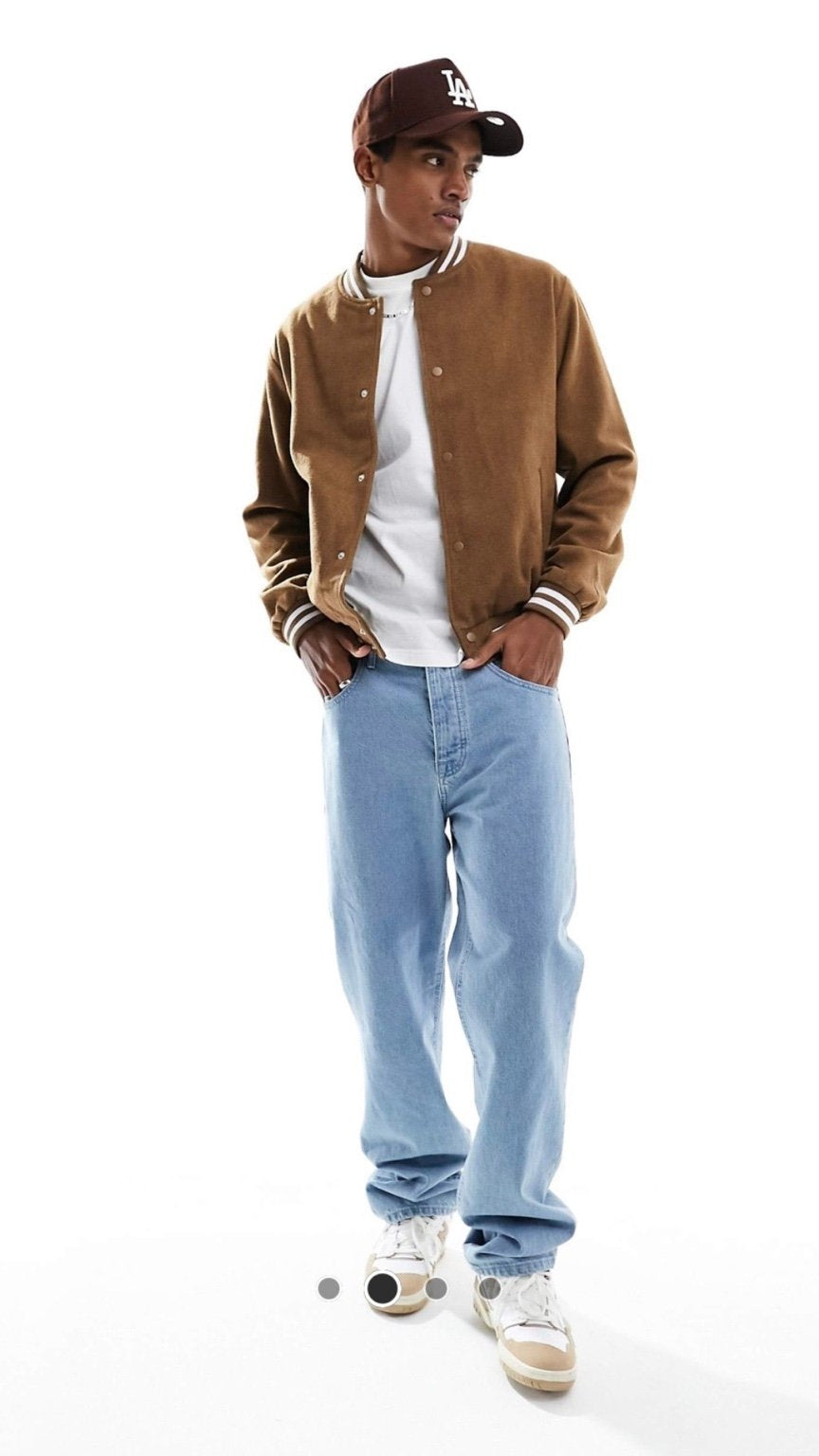 Person wearing a brown varsity jacket, white shirt, blue jeans, and a cap on a white background
