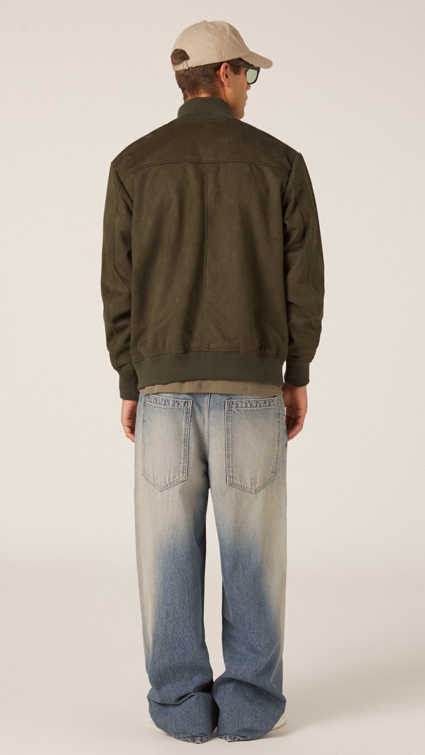 Person wearing a green jacket and blue jeans on a plain background