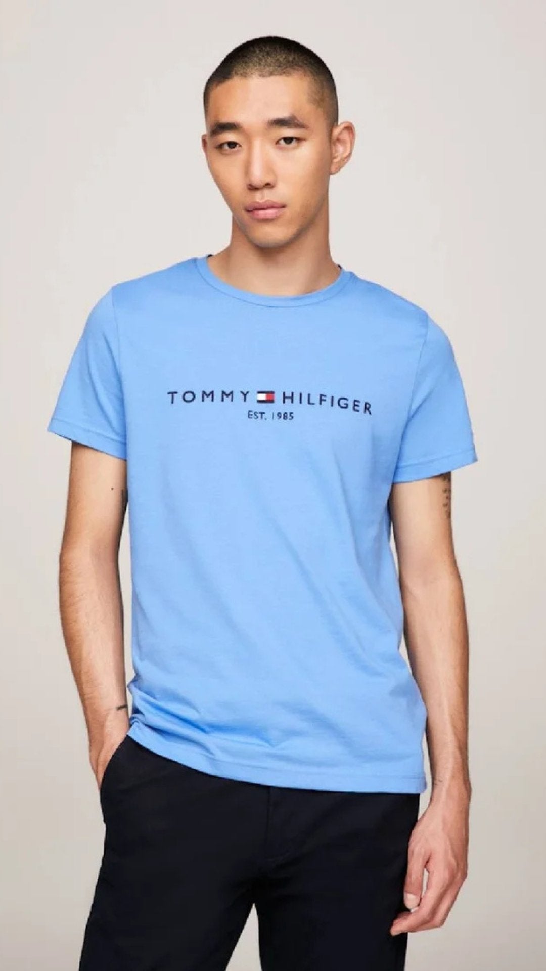 Person wearing a blue Tommy Hilfiger t-shirt on a plain background