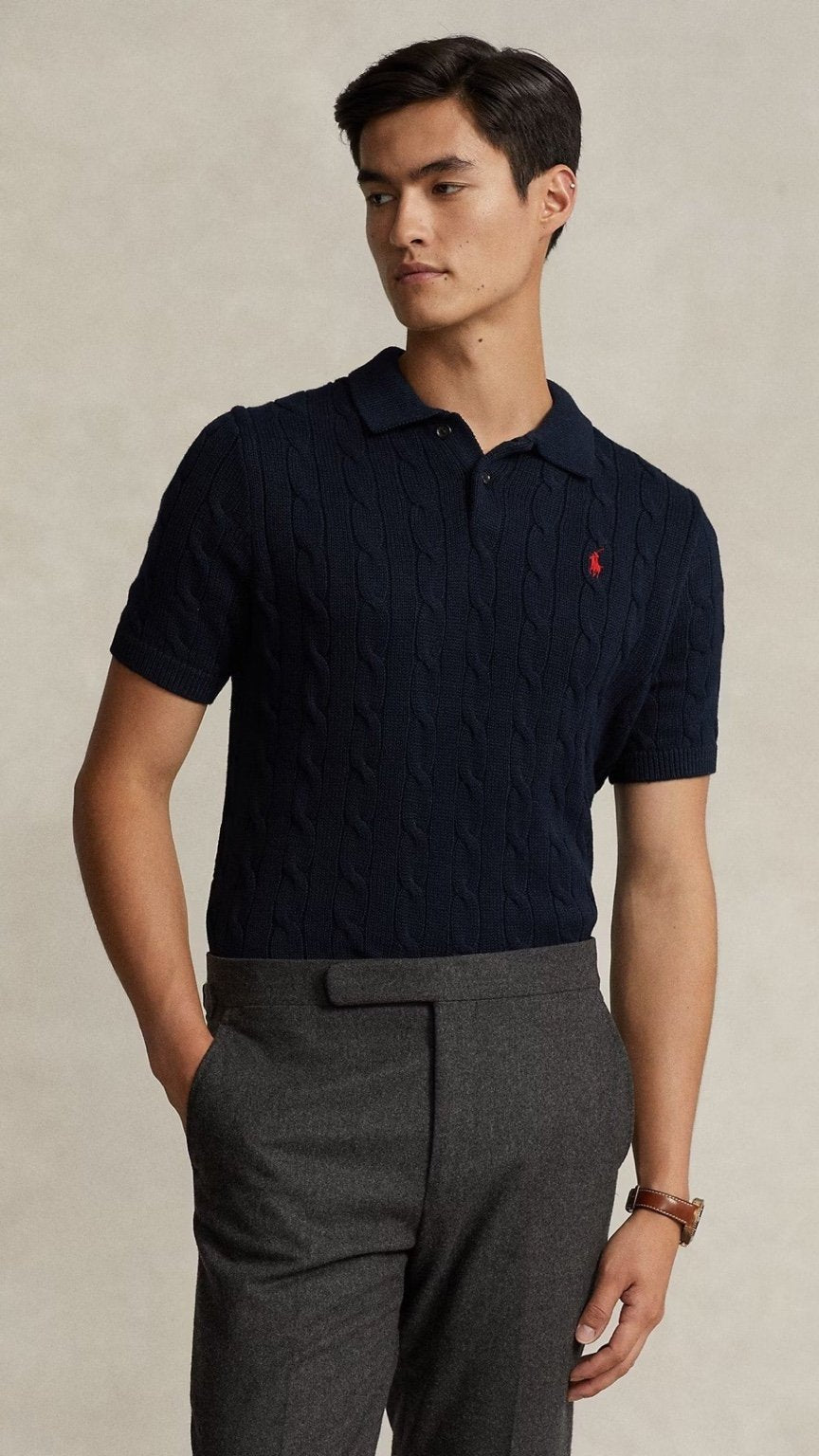 Man wearing a dark blue polo shirt with a red logo and gray pants on a beige background