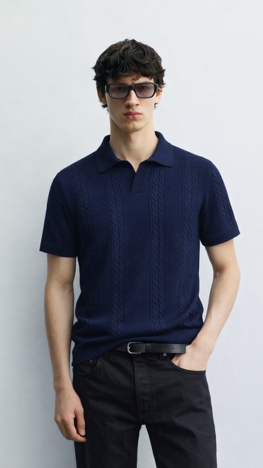 Man wearing a navy blue polo shirt and black pants against a white background