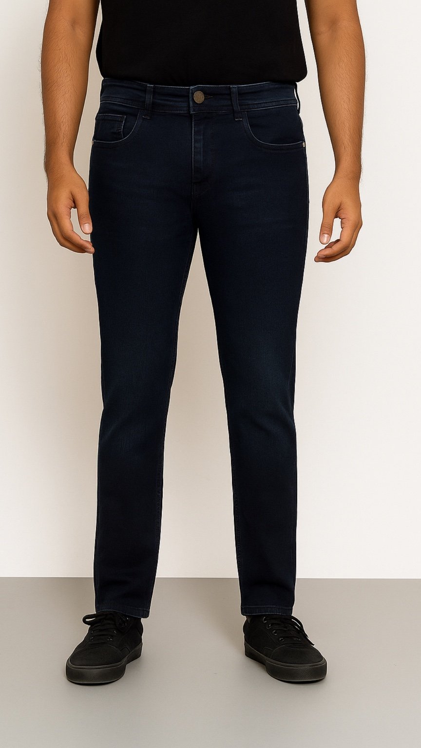 Person wearing dark blue jeans and black shoes on a plain background