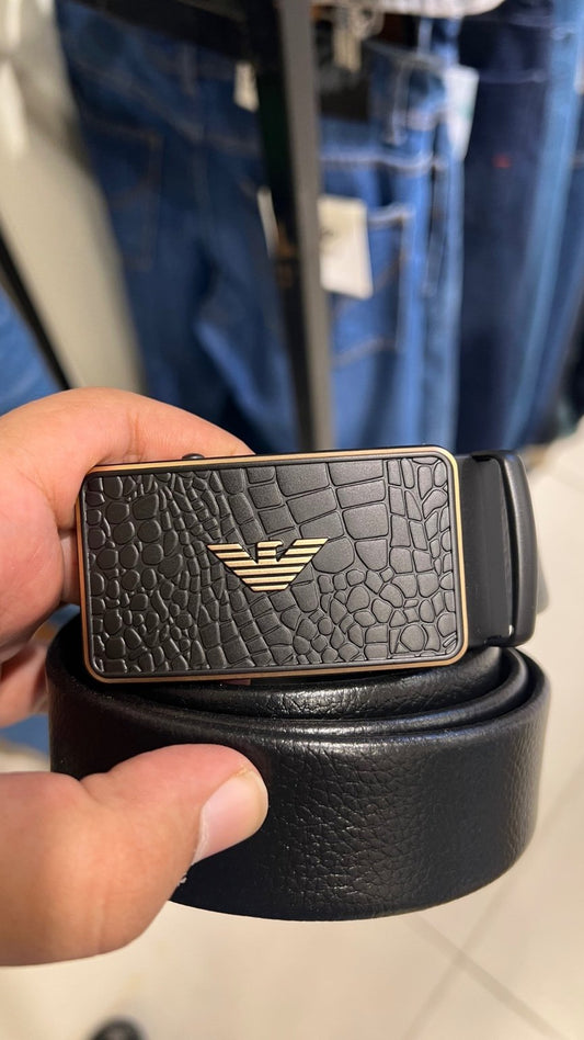 Black leather belt with a textured buckle held by a hand, with blue jeans in the background.