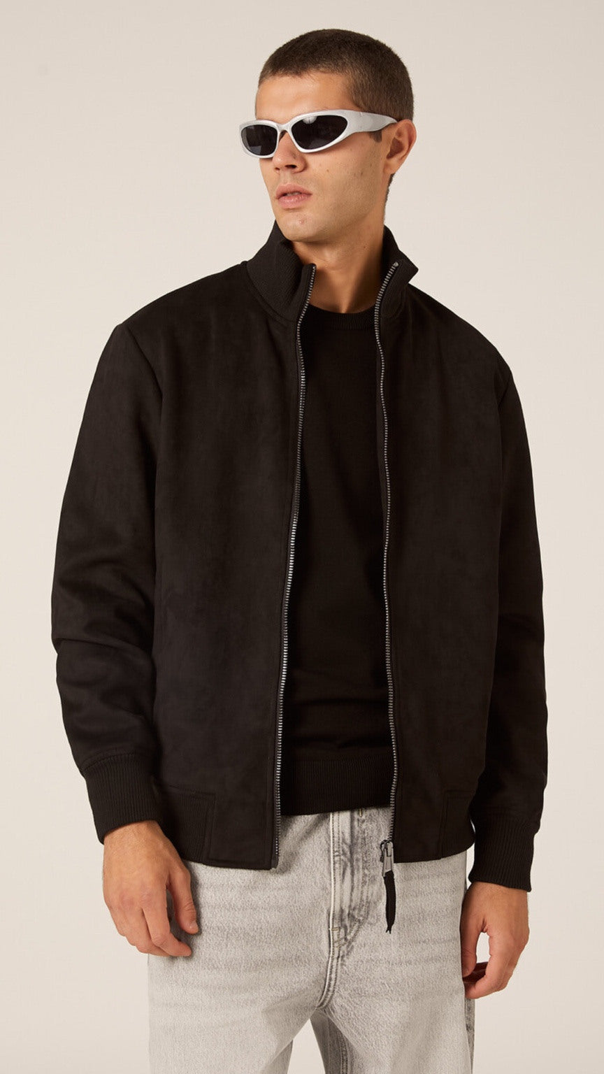 Man wearing a black jacket, black shirt, and light gray pants on a beige background