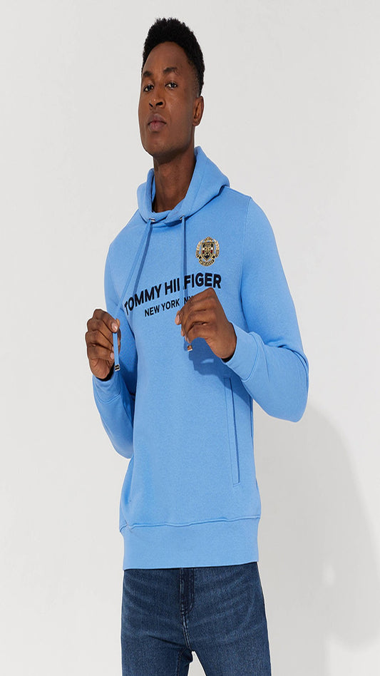 Person wearing a light blue hoodie with Tommy Hilfiger logo on a white background