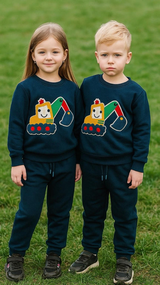 Two children wearing matching dark blue sweaters with colorful designs on a grassy background.