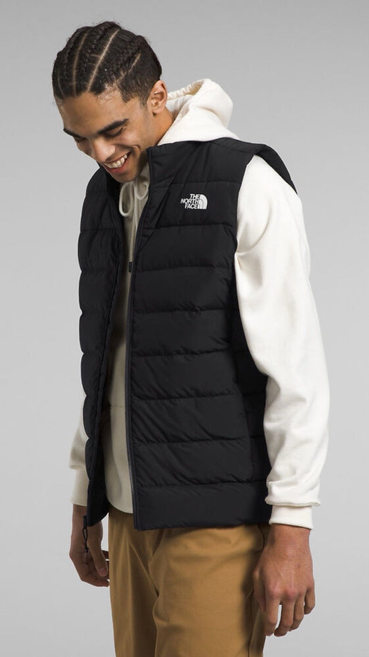 Man wearing a black puffer vest with The North Face logo on a gray background