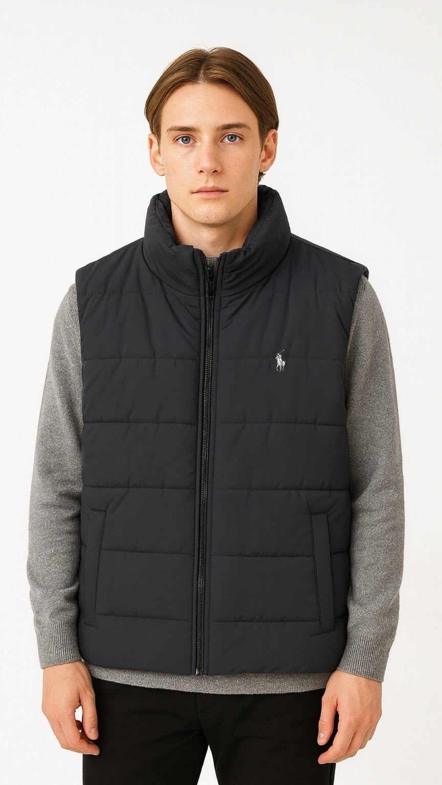 Man wearing a black quilted vest over a gray sweater on a white background