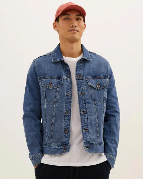 A male model wearing a blue denim jacket over a white t-shirt, paired with dark pants and a red cap.